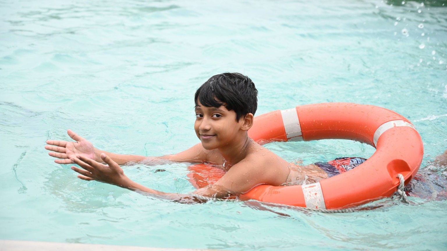 Niño nadando con un aro salvavidas en la piscina
